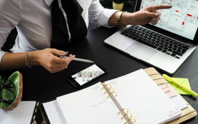 Un professionnel travaillant sur des plans de projets immobiliers à l'aide de plusieurs appareils dans un environnement de bureau.