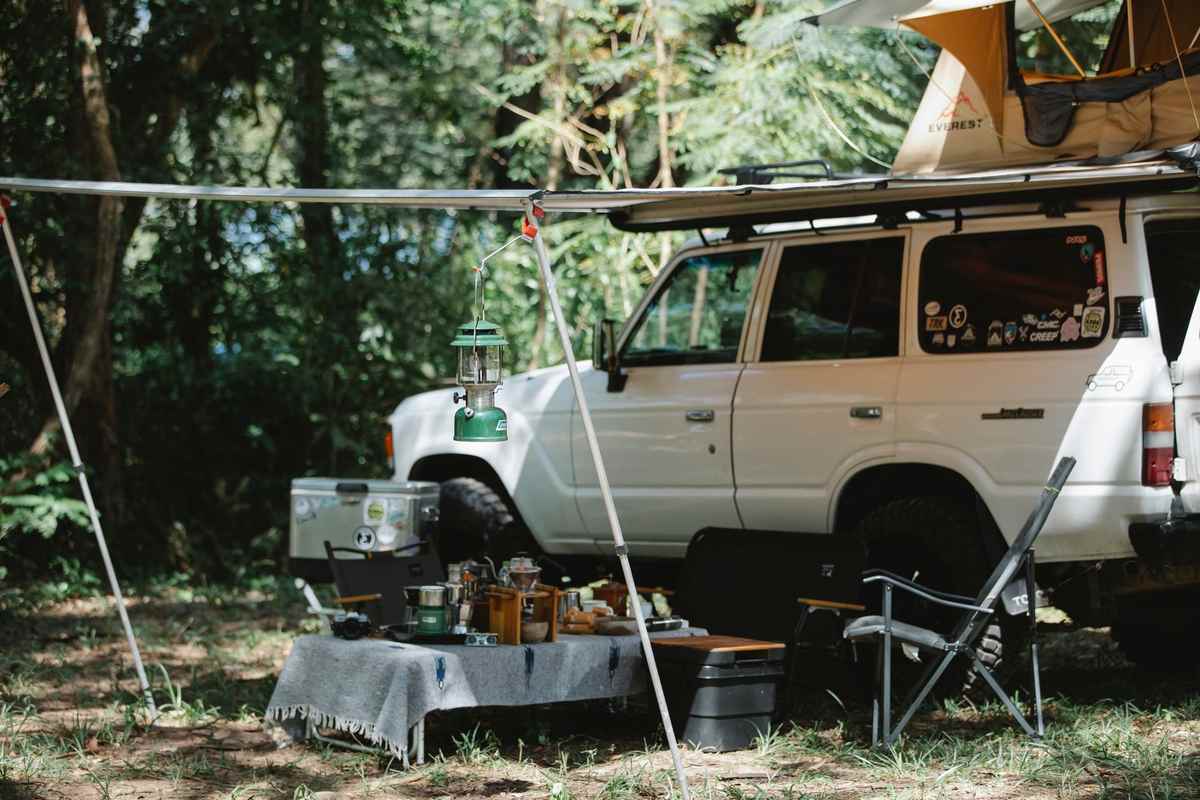Camper blanc avec tente et matériel de camping dans une forêt