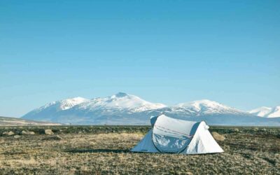 Tente blanche sur une prairie avec des montagnes enneigées en arrière-plan sous un ciel bleu