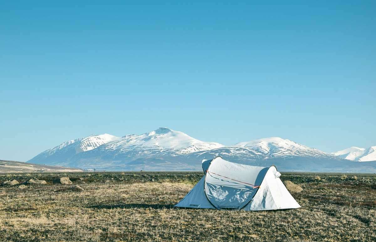 Tente blanche sur une prairie avec des montagnes enneigées en arrière-plan sous un ciel bleu