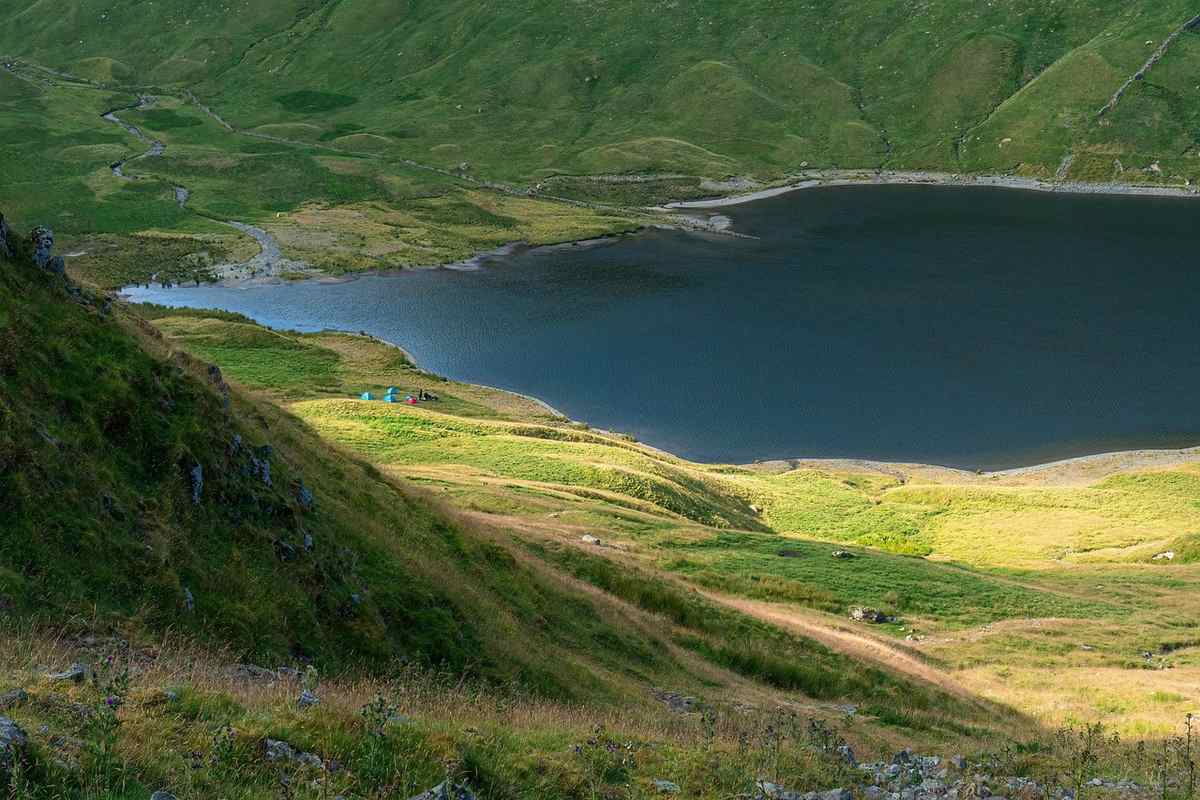 Un lac sombre entouré de collines herbeuses sous la lumière du jour Un lac sombre entouré de collines herbeuses sous la lumière du jour
