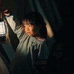 Fille asiatique dans une tente, lanterne allumée à la main, regard vers la gauche