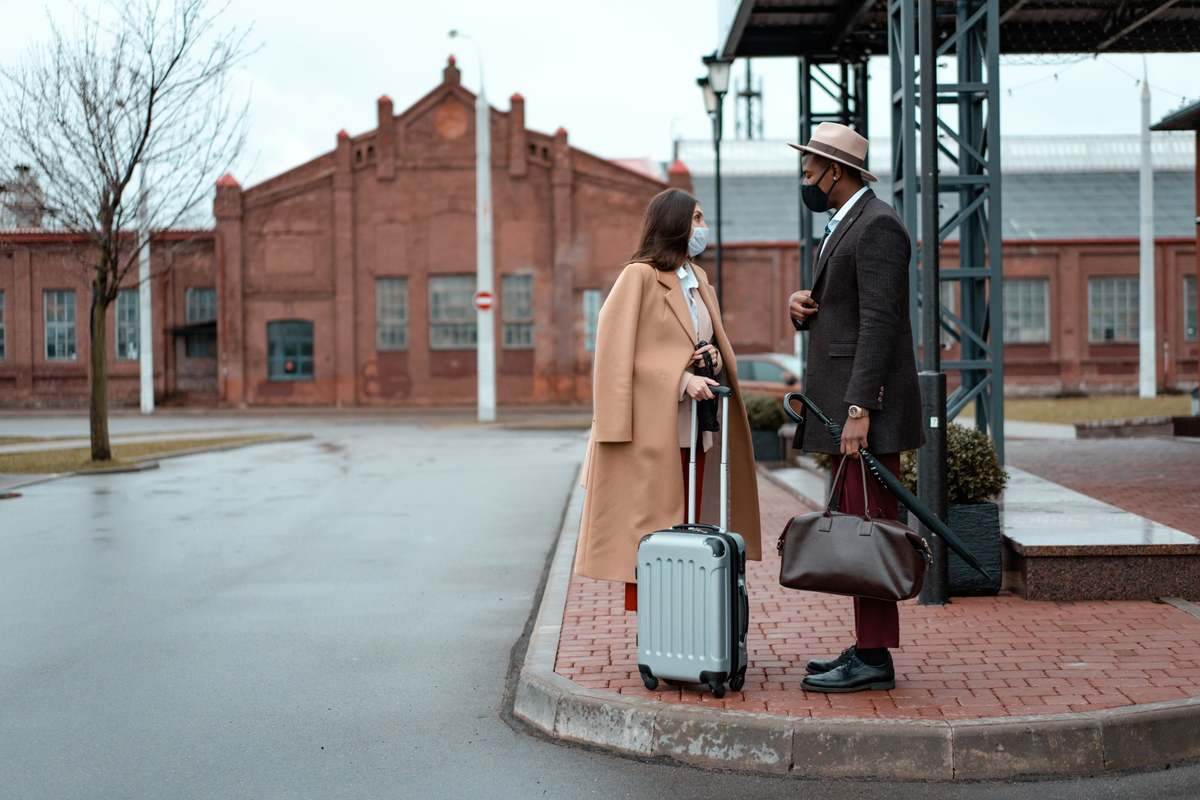 Deux voyageurs avec valise cabine et bagages devant architecture rouge urbaine Deux voyageurs avec valise cabine et bagages devant architecture rouge urbaine