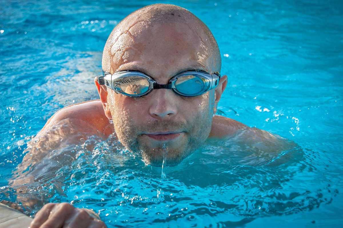 Homme portant des lunettes de natation, bras tendus dans l'eau, expression neutre