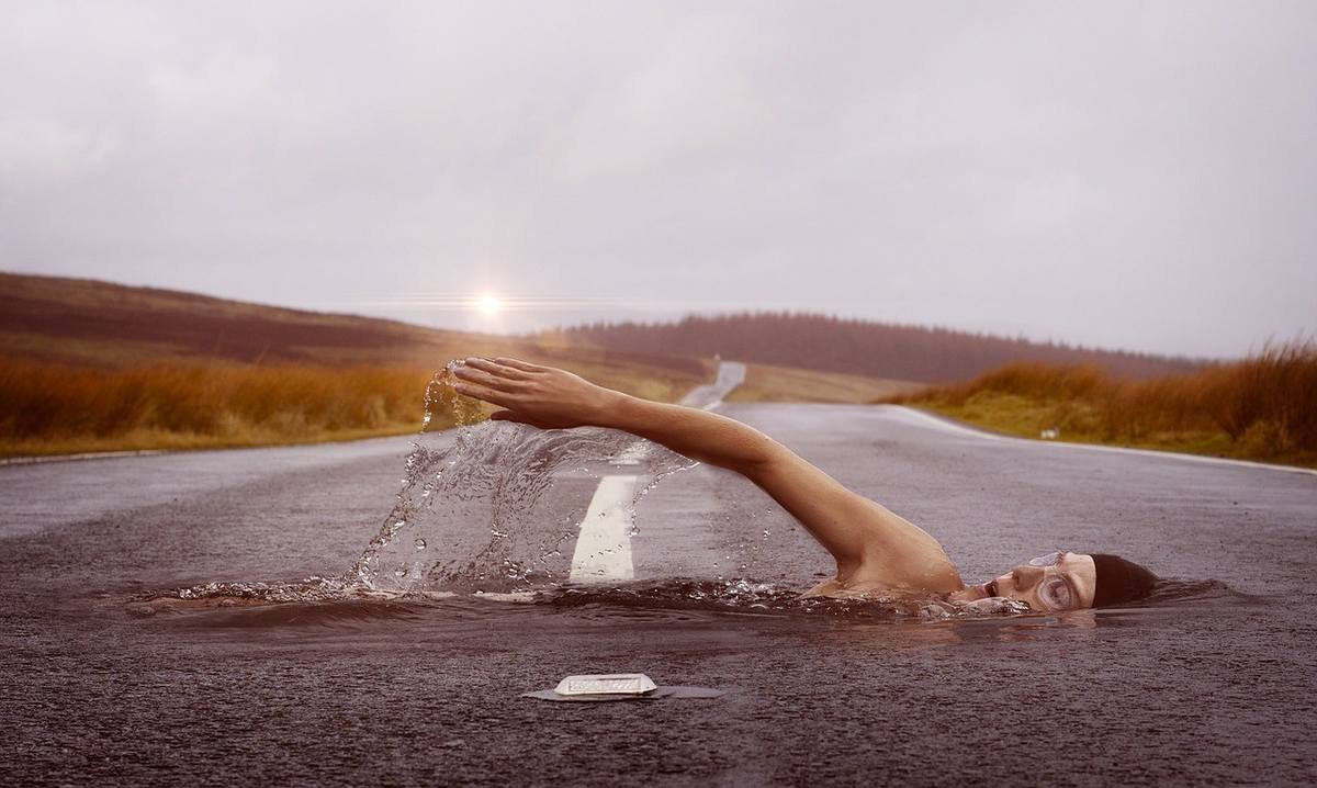 Une personne nage dans une route mouillée, bras tendu, eau en suspension, paysage rural, ciel nuageux Une personne nage dans une route mouillée, bras tendu, eau en suspension, paysage rural, ciel nuageux
