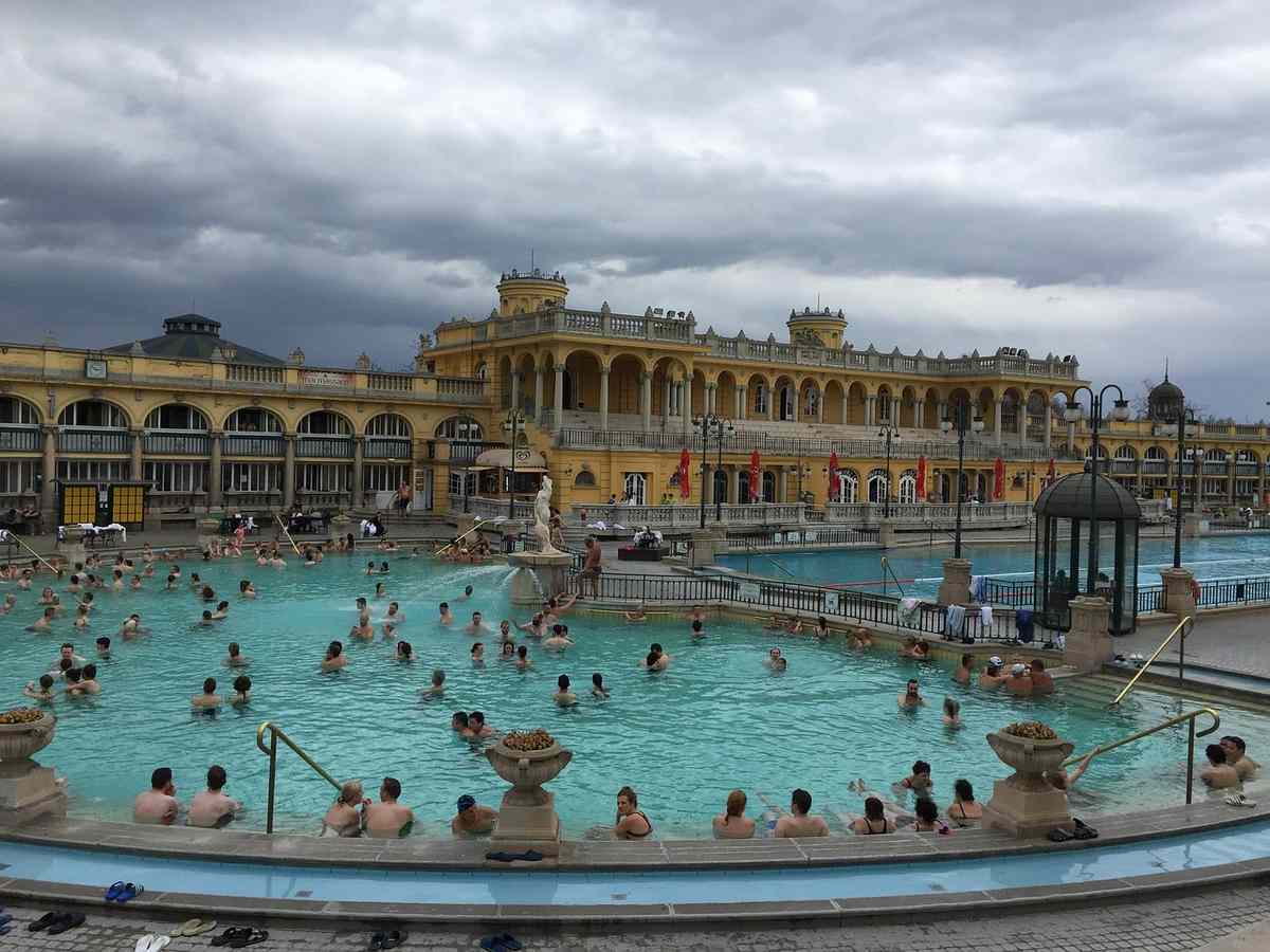 Baigneurs profitent d'un grand bassin thermal sous un ciel nuageux