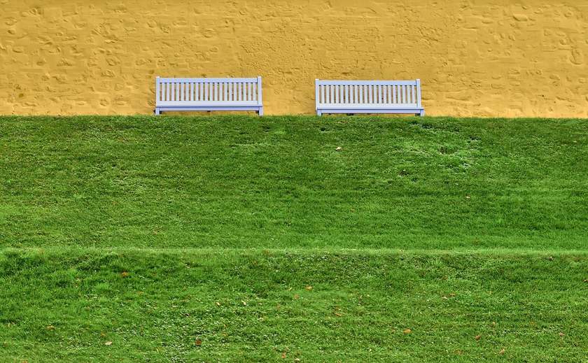 Bancs en bois sur une pelouse contre un mur jaune