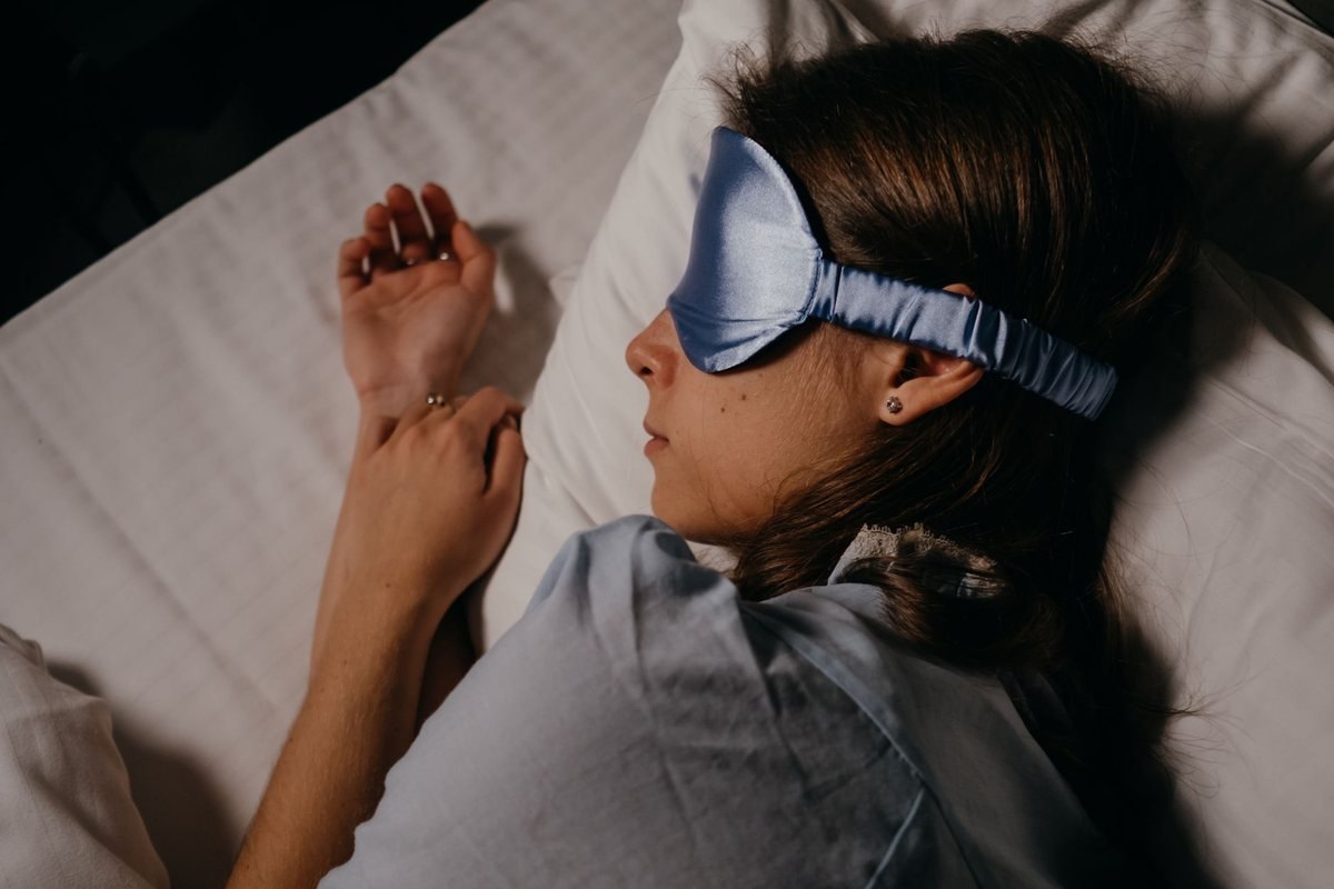 Femme endormie sous couette avec masque pour les yeux et oreillettes