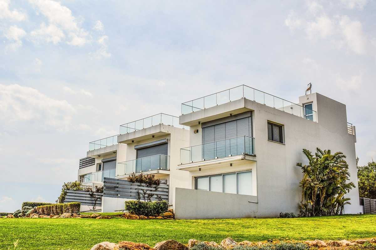 Maison blanche avec balcon, végétation et ciel nuageux