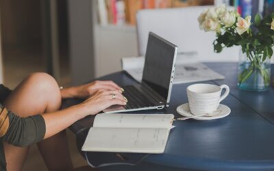 Une personne travaille sur ordinateur à table, avec tasse, cahier et fleurs